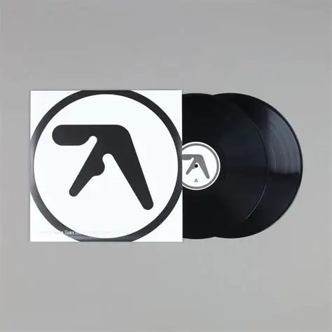 A vinyl record partially pulled from its sleeve, shown on a plain gray background. The sleeve is white with a large black circular logo, and the record is black with a matching center label.