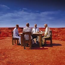 The album cover for Muse's Black Holes and Revelations features Four band members sitting around a table in a desert landscape with red sand and blue sky.